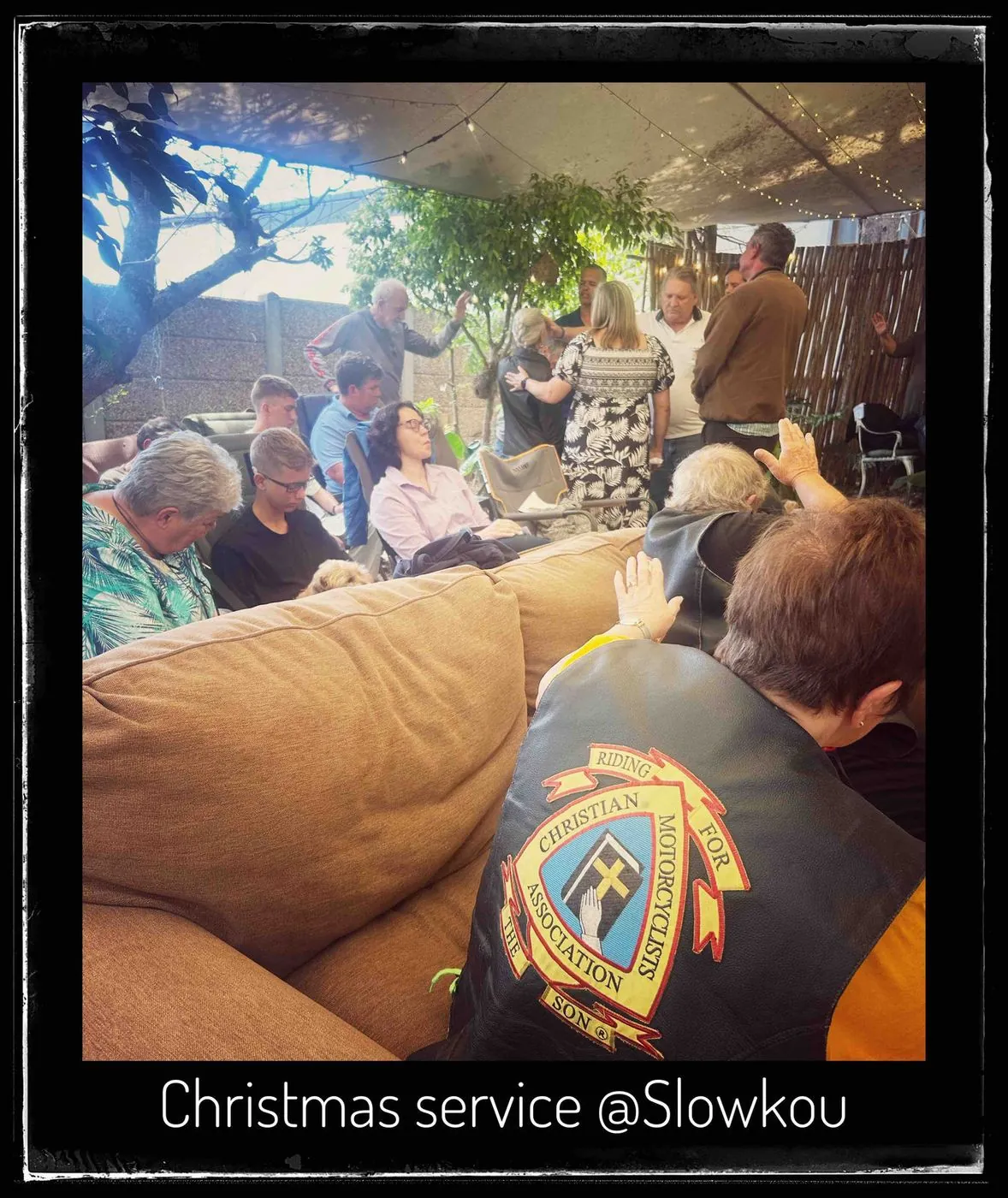 People sitting and standing in a room with a sofa, captioned Christmas service at Slowkou.