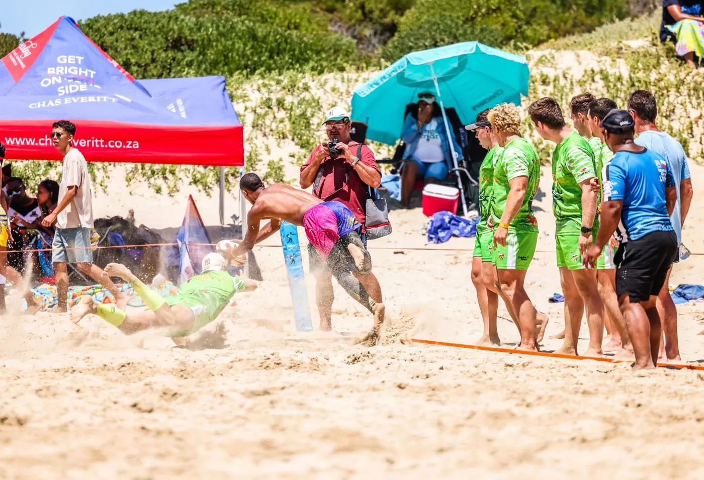 A crowded beach with tents and players in green bibs.
