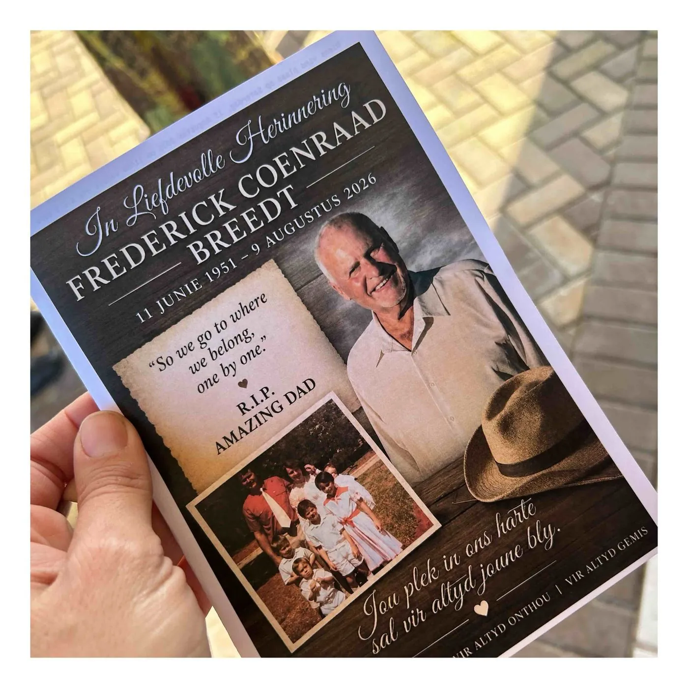 A hand holds a printed memorial programme with a portrait of an older man in a hat, headed In liefdevolle herinnering for Frederick Coenraad Breedt.