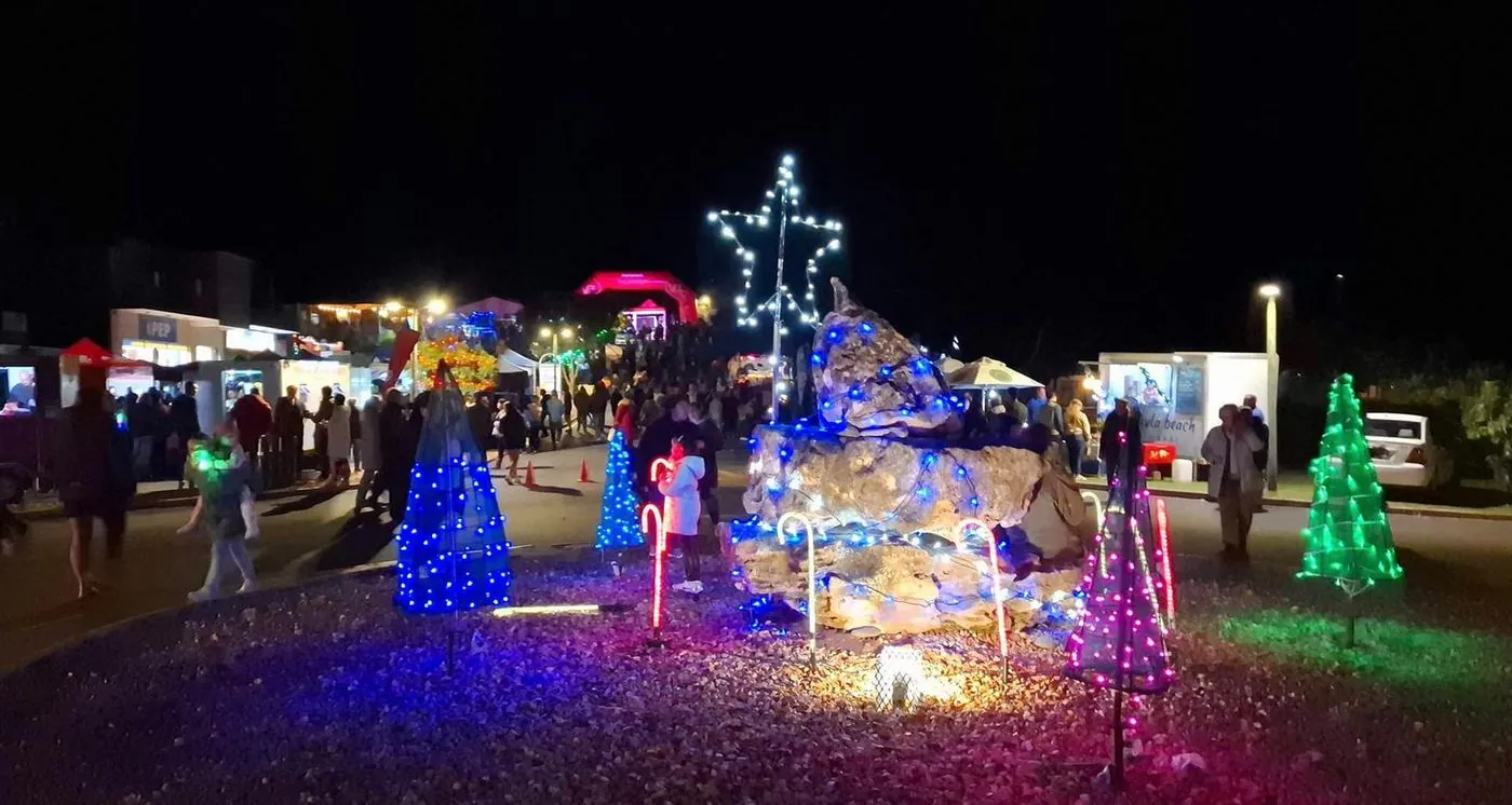 A night-time market with stalls and a Christmas tree outlined in coloured lights.