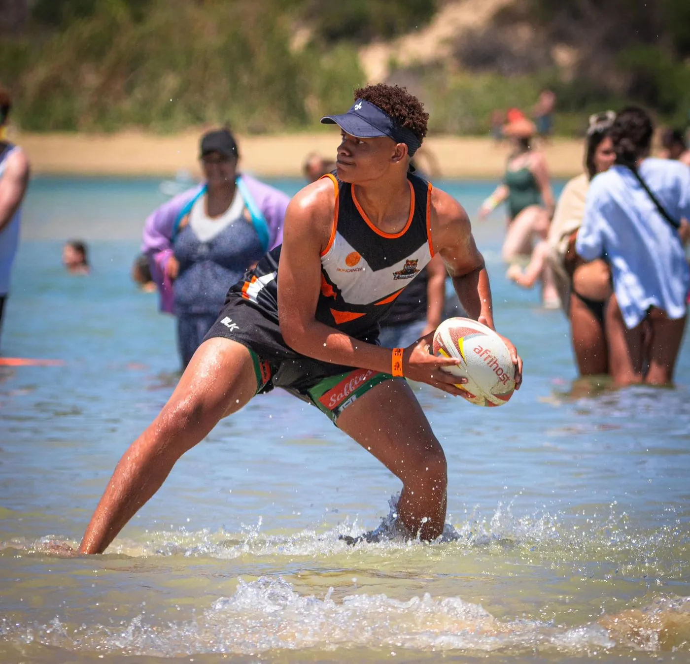 A woman holds a rugby ball while wading through a river.