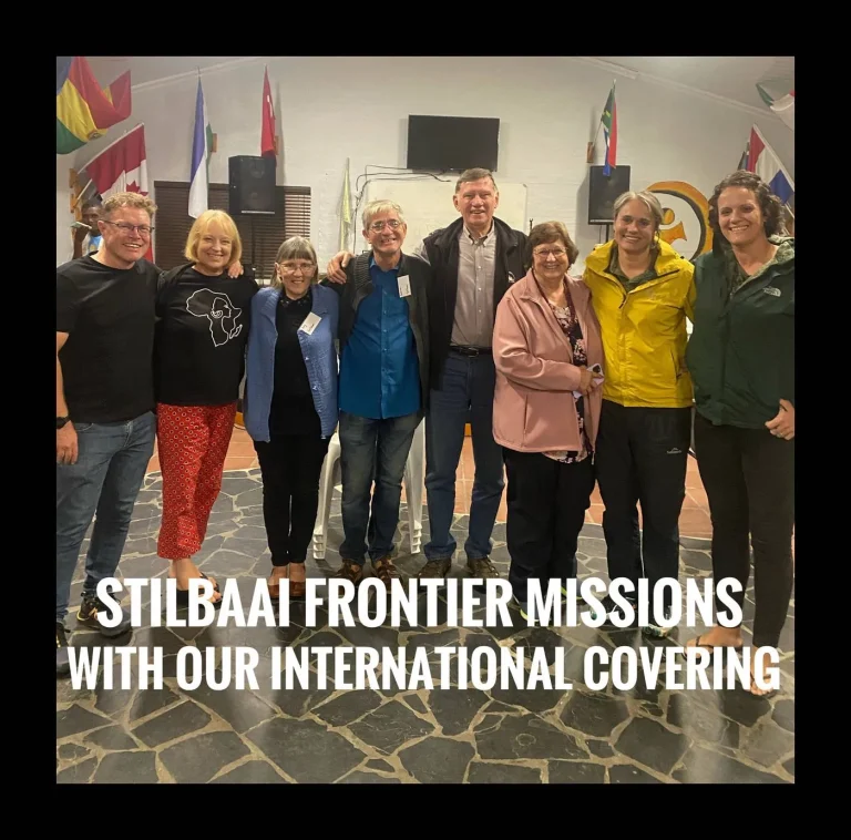 About a dozen people standing in front of national flags, captioned Stilbaai Frontier Missions with our international covering.