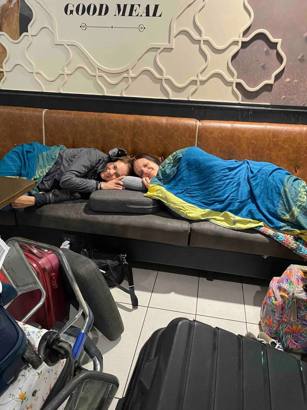 Two people sleeping on a leather sofa beside luggage.