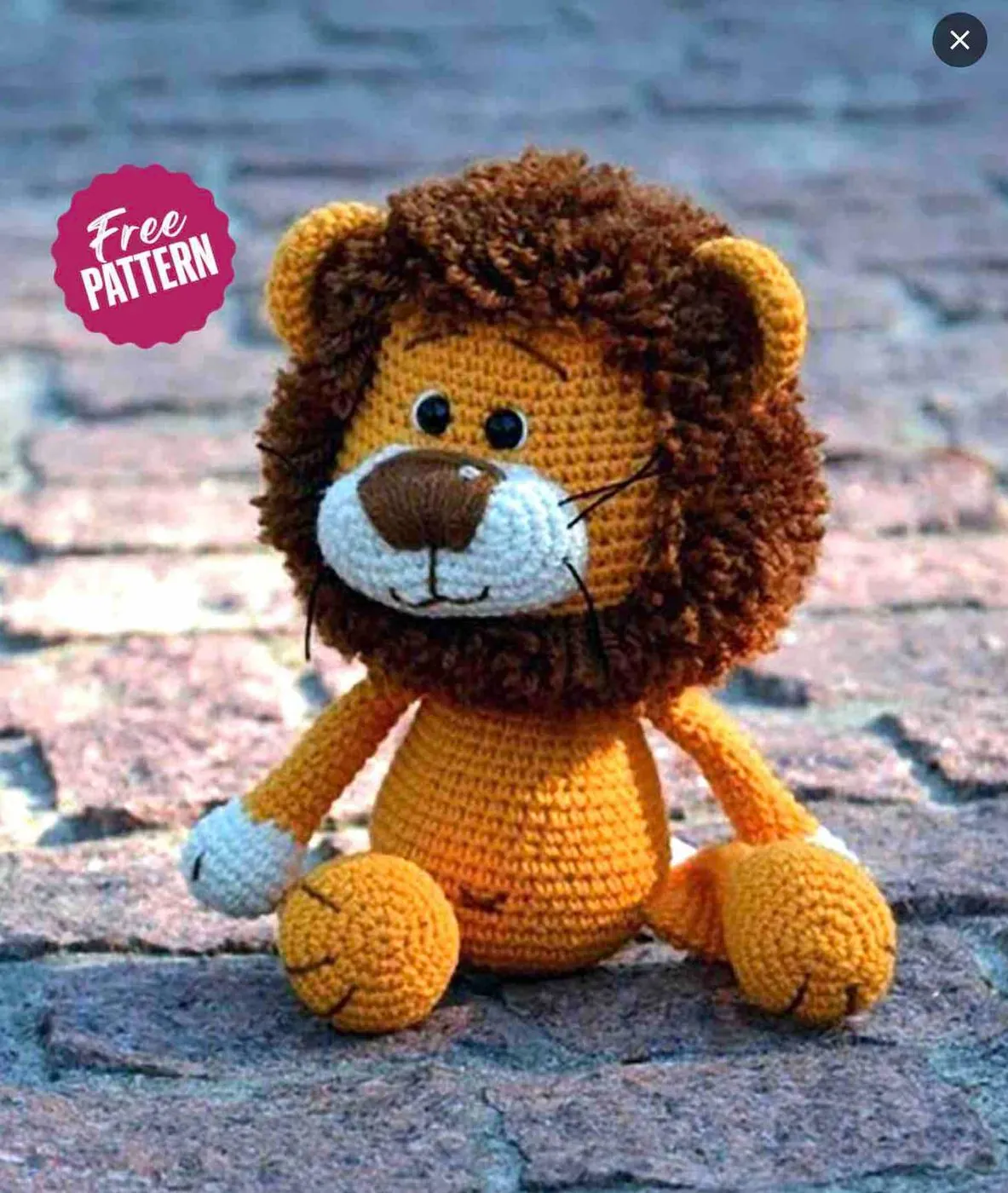 A crocheted lion toy sitting on a stone surface, with a Free pattern label.