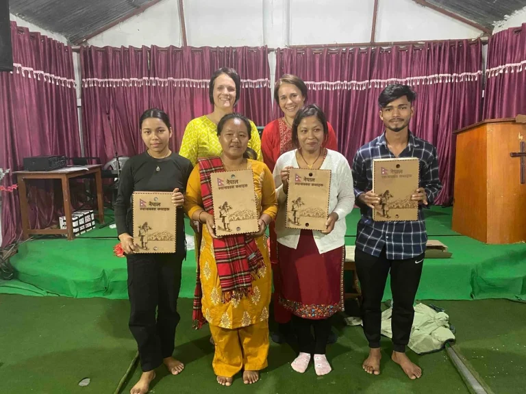 Five people standing on a stage holding wooden boxes, with a curtain behind them.