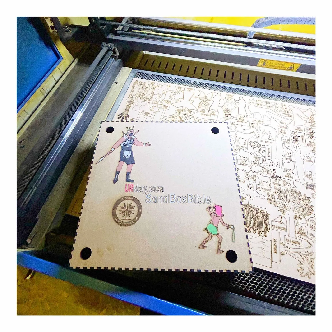 A laser cutter with an engraved wooden sheet of small drawn figures on its bed.