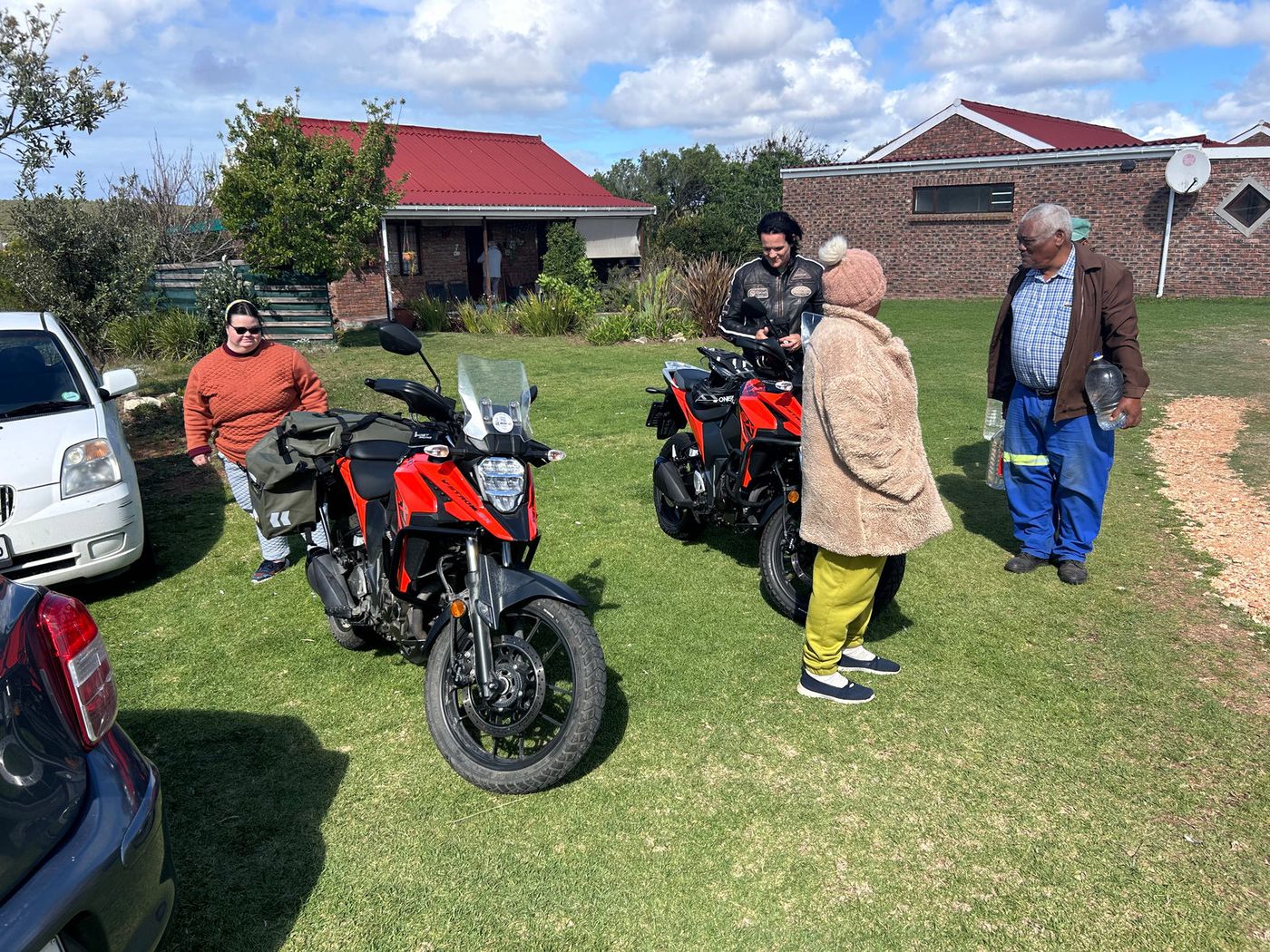 A red motorbike on a lawn with several people standing near a house.