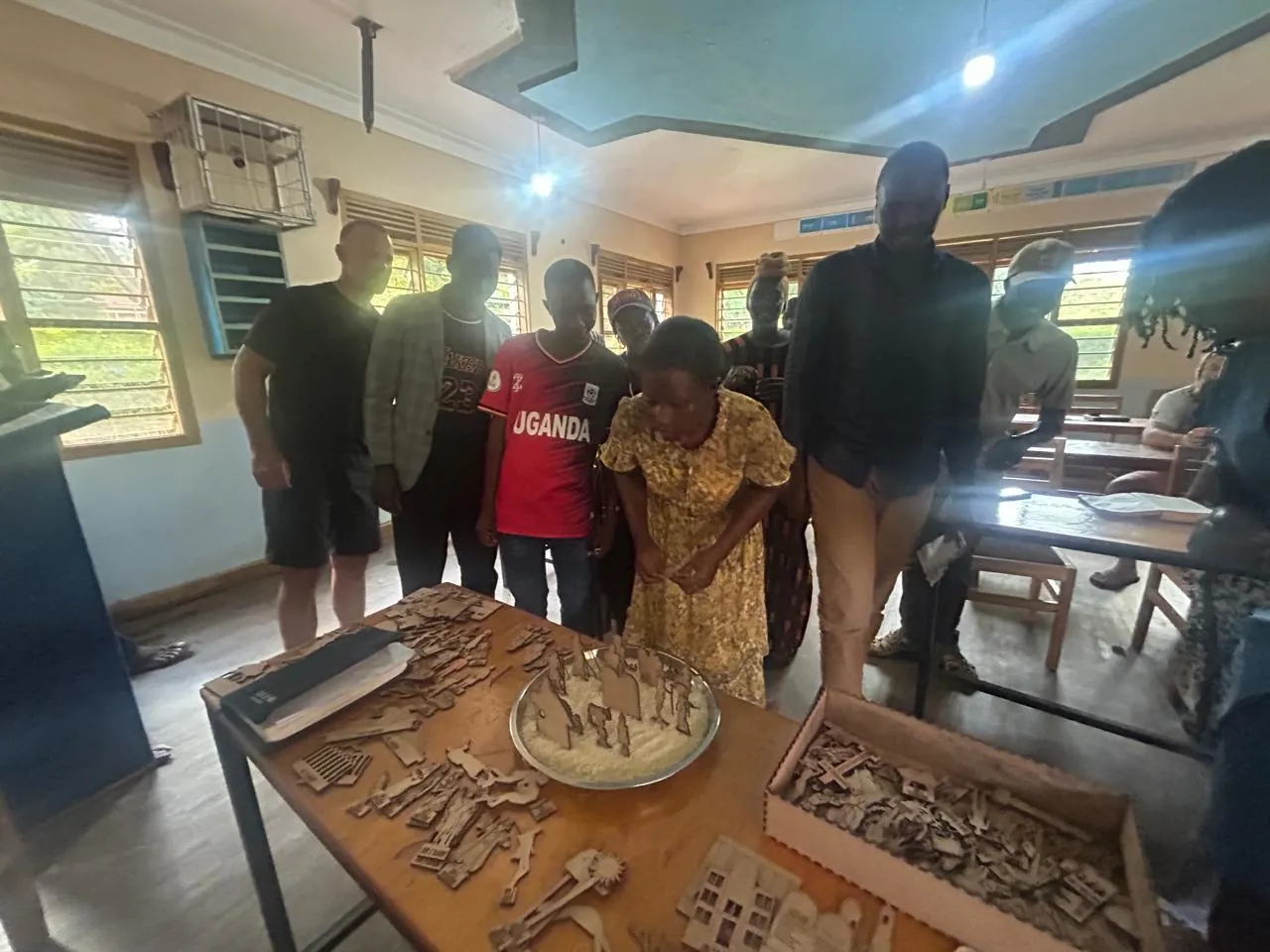 A wooden table covered in small flat wooden Bible figures and an open wooden box, with a group of adults and children standing around it in a classroom.