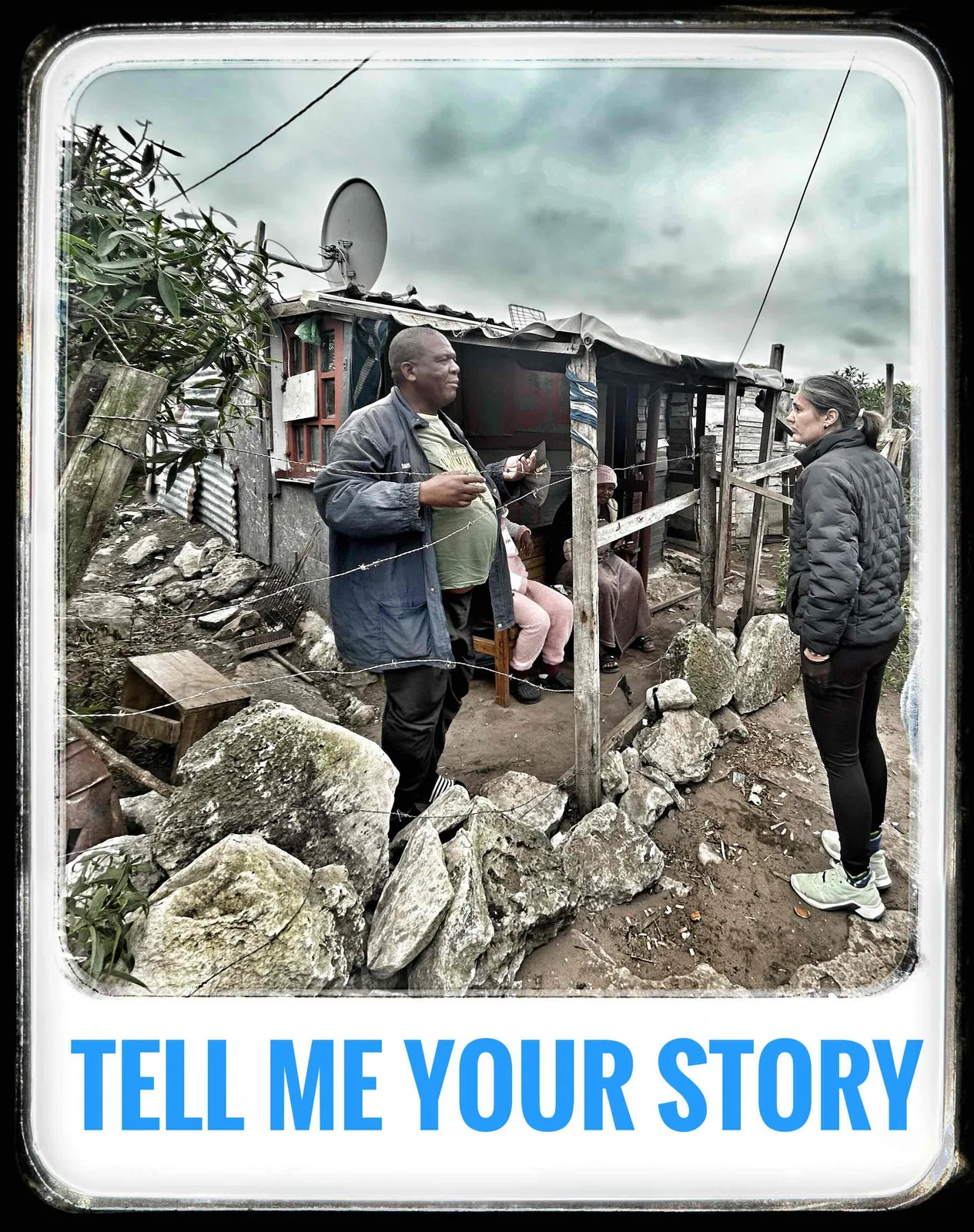 Two people talking outside a rock-built shack with a satellite dish, captioned Tell me your story.