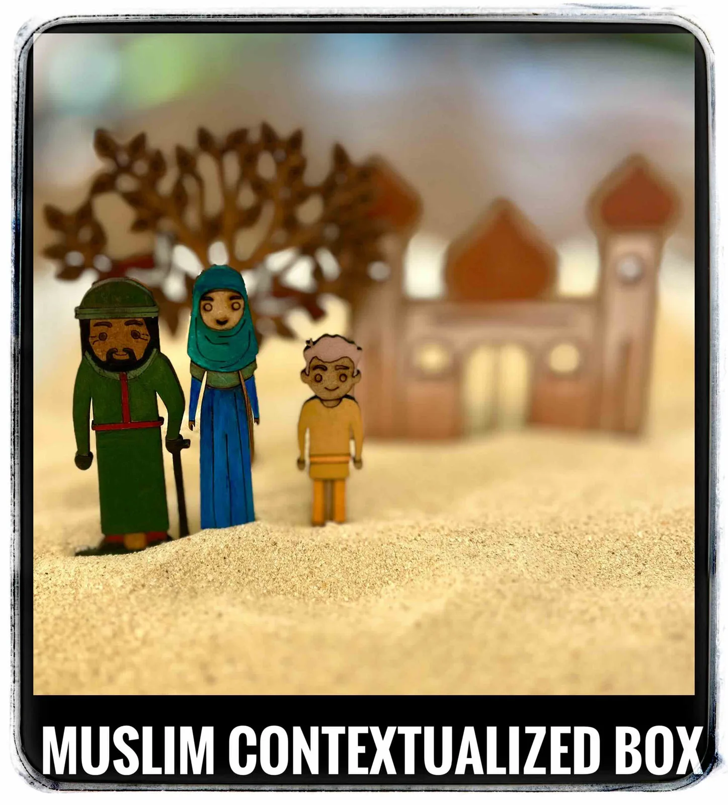 Painted wooden figures of three people in Muslim dress standing in sand with a blurred mosque behind them, captioned Muslim contextualized box.